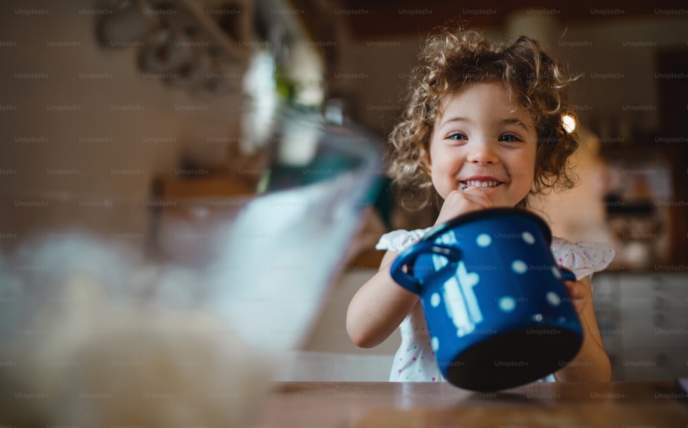 Una niña feliz sentada en la mesa en el interior de casa, comiendo espaguetis y mirando a la cámara.