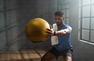 A young African American sportsman standing and lifting a medicine ball indoors, workout training concept.