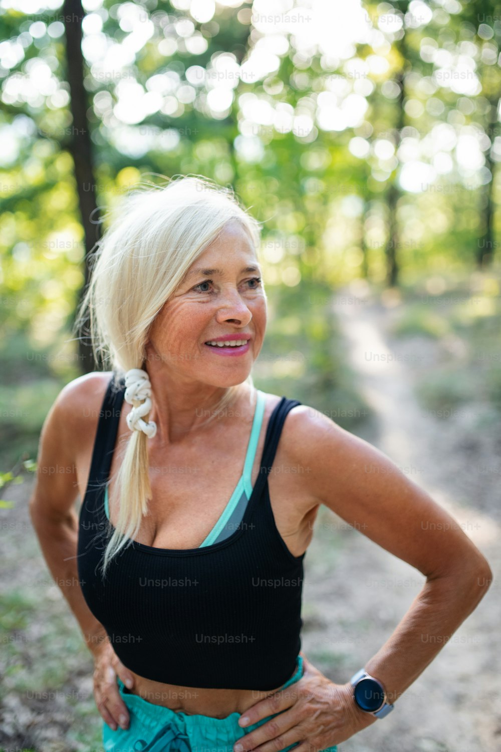 A portrait of active senior woman runner standing outdoors in forest.