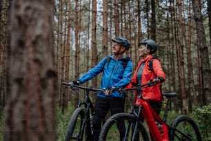 Una pareja de ciclistas mayores con bicicletas eléctricas admirando la naturaleza al aire libre en el bosque en un día de otoño.