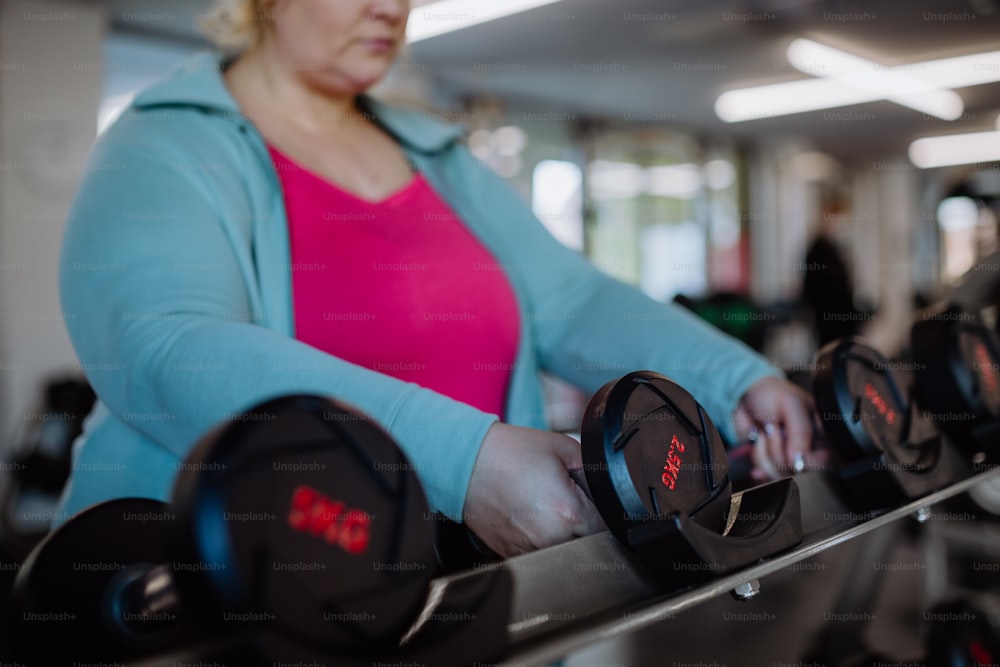 An unrecognizable plus size woman training taking dumbbells indoors in gym