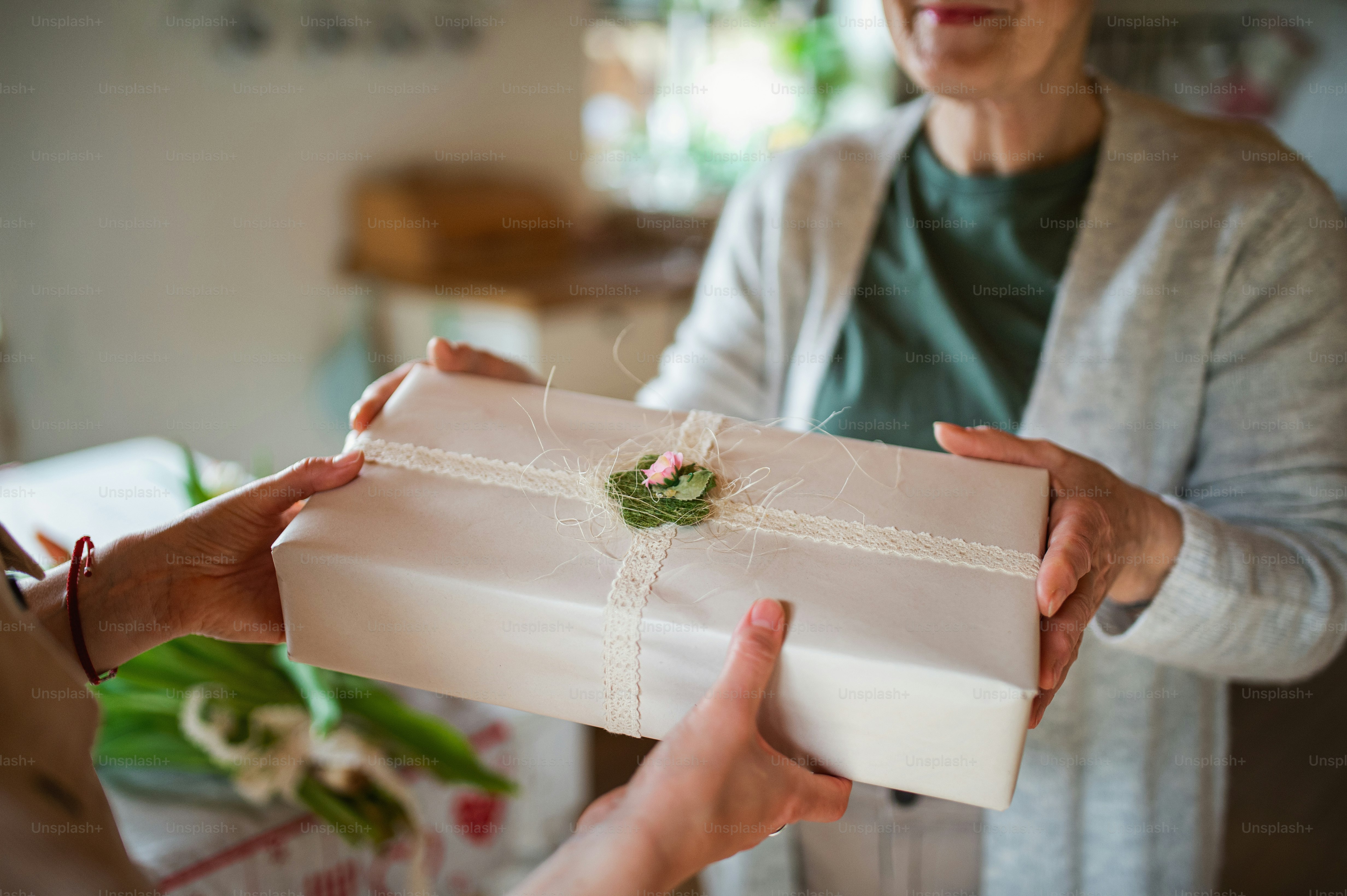 Un primer plano de una hija adulta irreconocible que se convierte en un regalo para una madre mayor en el interior de la casa, el día de la madre o la celebración del cumpleaños.