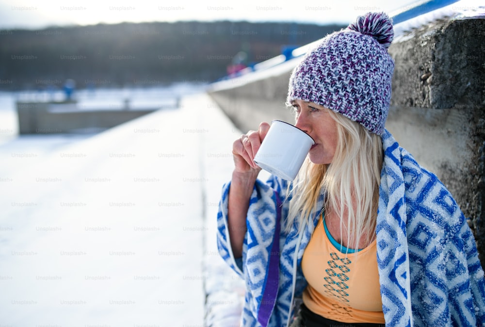 A portrait of active senior woman sports clothes drinking tea outdoors in winter, cold therapy concept. Copy space.