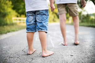 A rear view of legs of two barefoot unrecognizable small boys hopscotching on a road in park on a summer day.