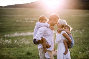 Happy young family with small children spending time together outside in green summer nature at sunset.