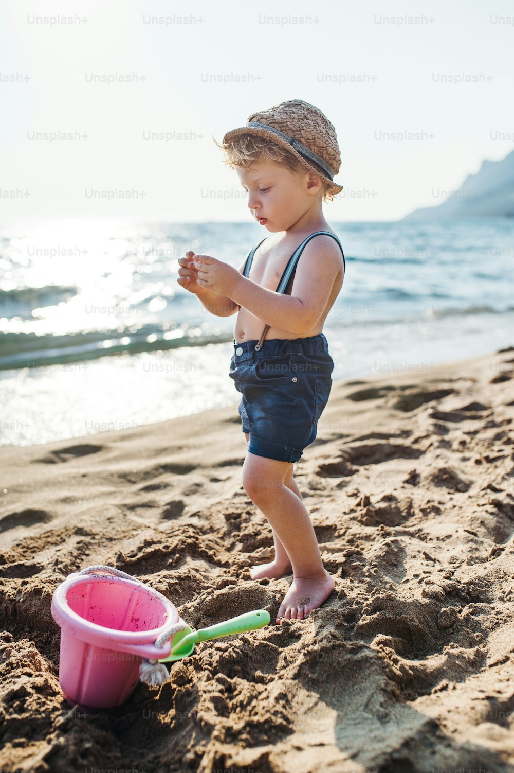 Un niño pequeño ocupado sentado en la playa en vacaciones de verano, jugando.