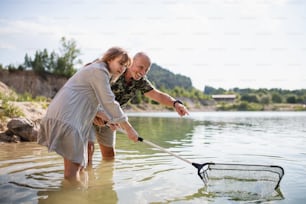 Happy preteen girl and senior grandfather with fishing net on summer holiday by lake.