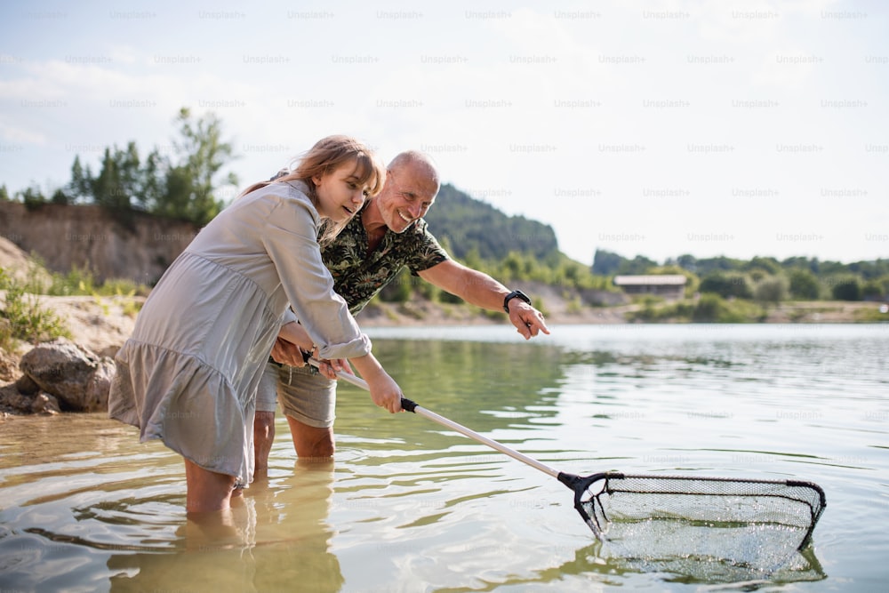 Menina pré-adolescente feliz e avô sênior com rede de pesca nas férias de verão pelo lago.