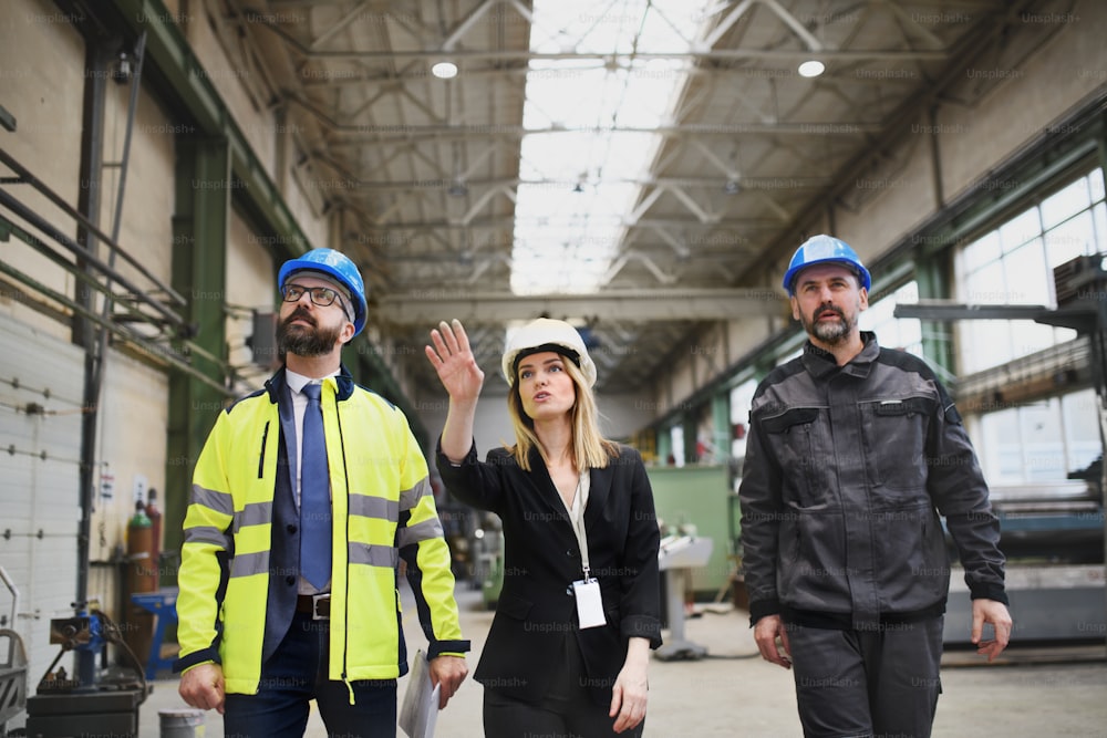 Manager supervisors and industrial worker in a uniform walking in large metal factory hall and talking.