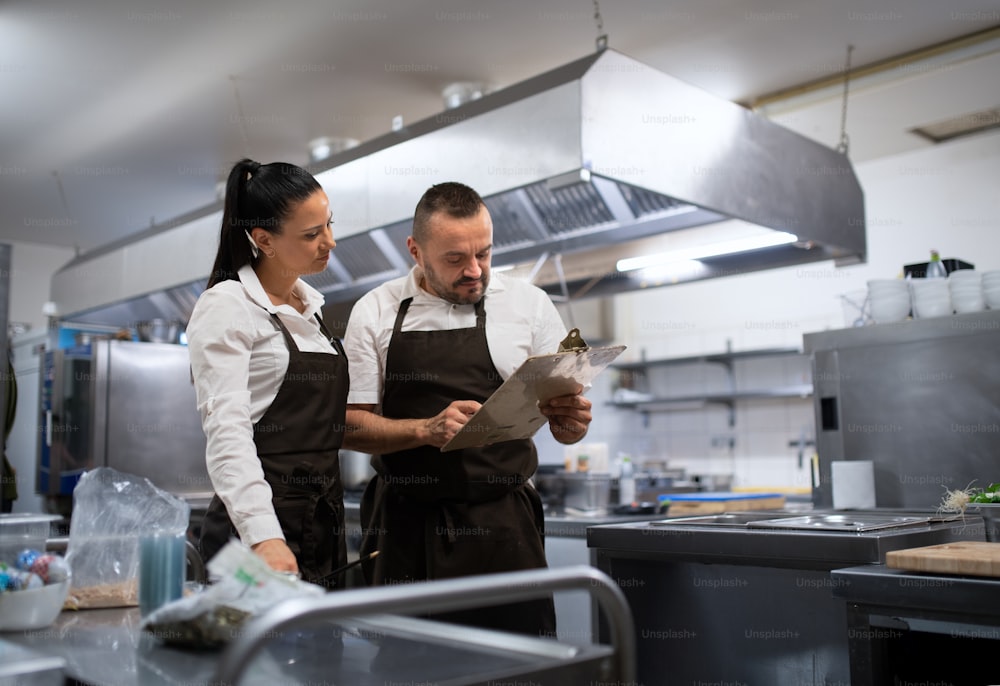 A chef and cook discussing menu indoors in restaurant kitchen.