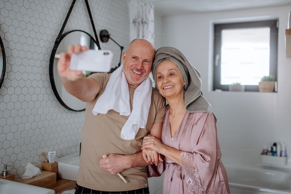Un couple de personnes âgées amoureux dans la salle de bain, à l’aide d’un smartphone, concept de routine matinale.