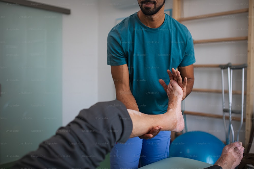 Un primo piano del fisioterapista che si esercita con la gamba di un paziente anziano in una stanza fisica.