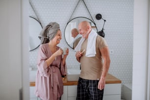 A senior couple in bathroom, brushing teeth and talking, morning routine concept.