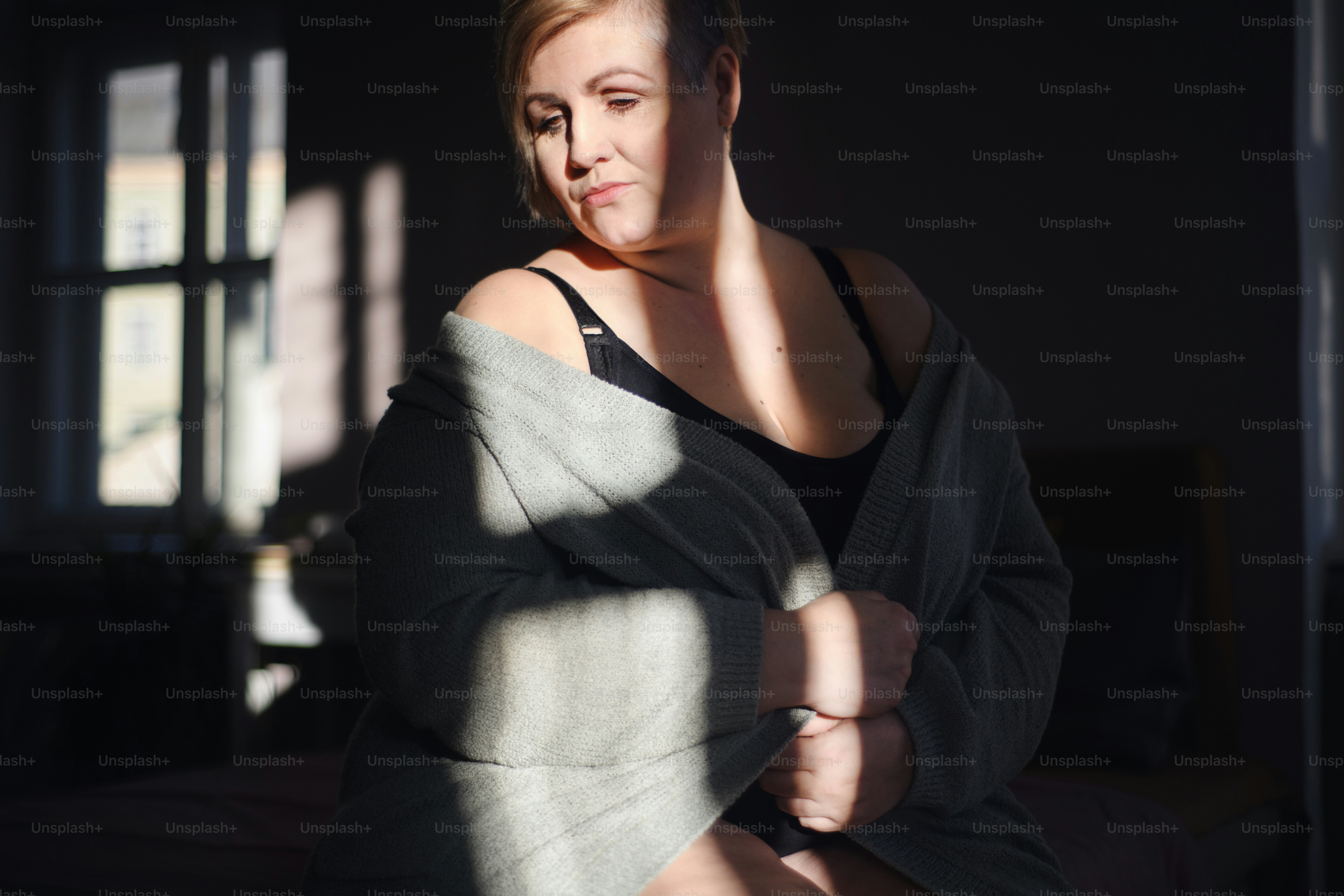 A depressed lonely fat woman in underwear looking down and thinking at home.