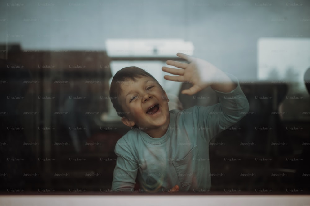 A happy little boy waving through window to say goodbye when travelling in train.