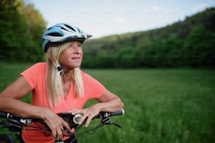 A cheerful active senior woman biker outdoors in nature.