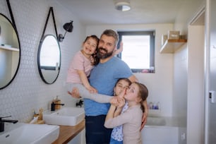 A father bonding with his three little daughters in bathroom and looking at camera.