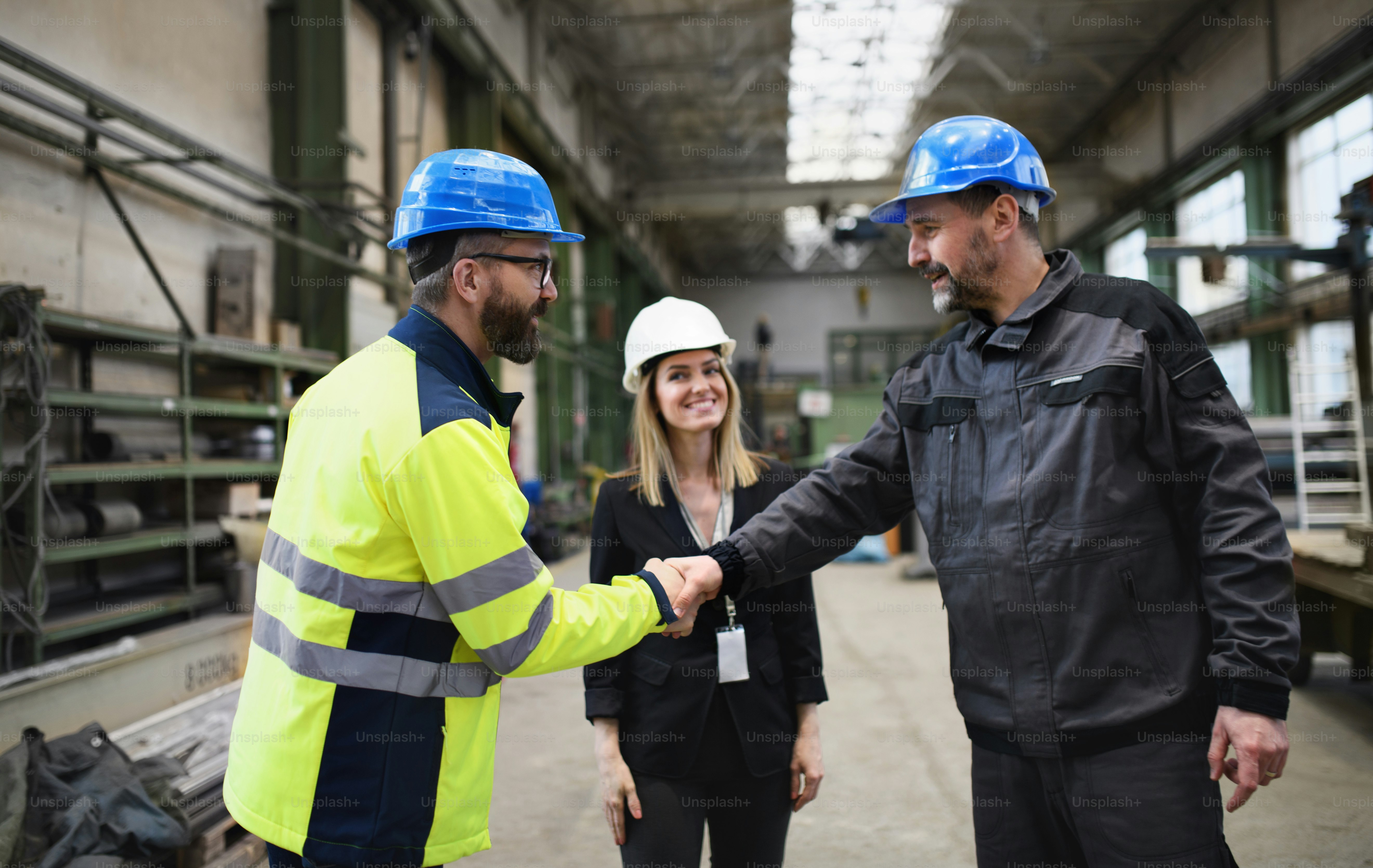 An engineer and industrial worker in uniform shaking hands in large ...
