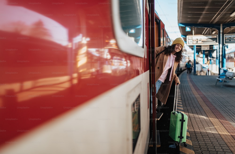 Uma jovem mulher viajante feliz com bagagem saindo do trem na plataforma da estação de trem