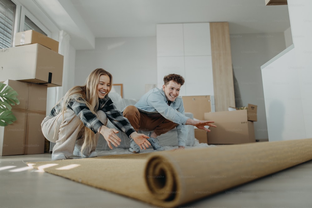 A cheerful young couple in their new apartment, rolling out carpet. Conception of moving.