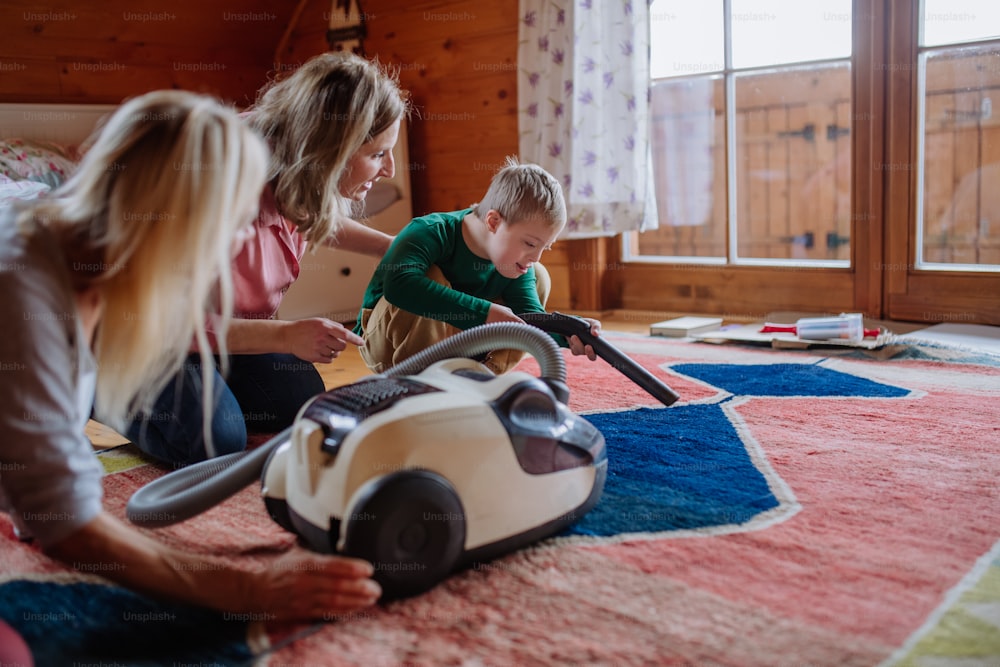 A boy with Down syndrome with his mother and grandmother vacuum cleaning at home