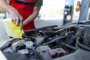 A car mechanic replacing and pouring oil into engine at maintenance repair service station