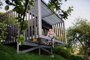 Um jovem casal sentado e abraçado no terraço da rede em sua nova casa em pequena casa em bosques, conceito de vida sustentável.