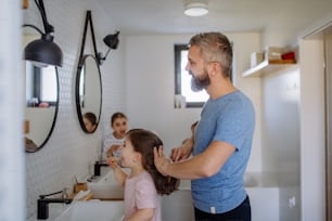 A father brushing his little daughter's hair in bathroom, morning routine concept.