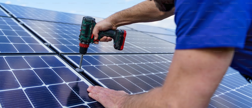 A man worker installing solar photovoltaic panels on roof, alternative energy concept. Close up hands with drill.