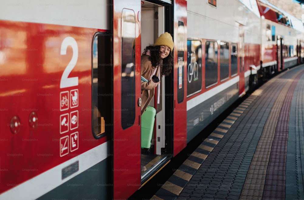 Una giovane donna viaggiatrice felice con i bagagli che scende dal treno alla piattaforma della stazione ferroviaria