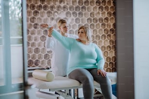 Una donna fisioterapista adulta media che si esercita con una donna in sovrappeso all'interno del centro di riabilitazione