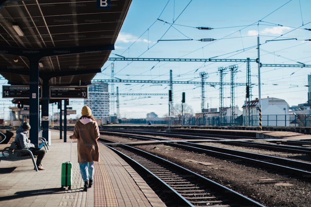 Una giovane viaggiatrice felice con i bagagli in attesa del treno alla piattaforma della stazione ferroviaria