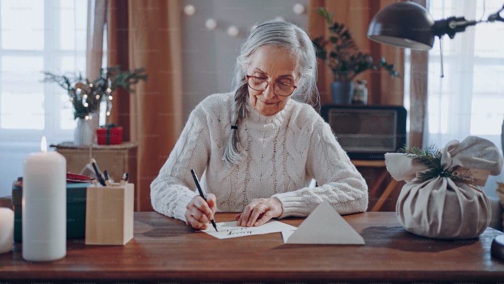 Eine glückliche ältere Frau, die zu Hause Weihnachtskarten schreibt