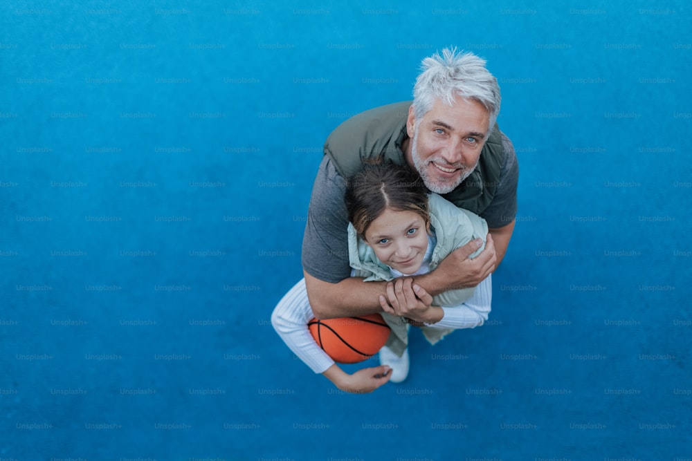 Un père et sa fille adolescente jouant au basket-ball à l’extérieur sur le terrain, vue en plongée.