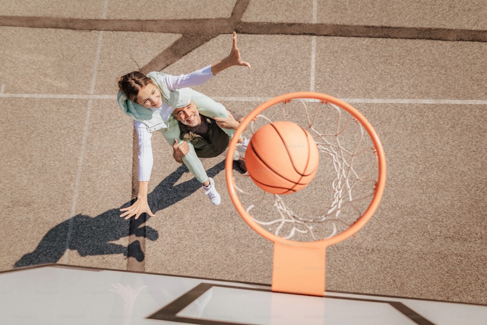 A father and teenage daughter playing basketball outside at court, high angle view above hoop net.A father and teenage daughter playing basketball outside at court, high angle view above hoop net.A happy father and teen daughter playing basketball outside at court, high fiving.