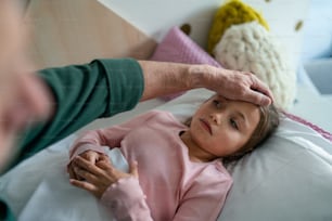 A grandfather taking care of his ill granddaughter lying in bed.