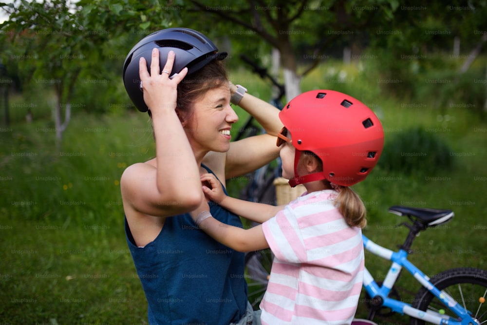 Una familia joven con niños pequeños preparándose para andar en bicicleta, poniéndose cascos frente a la casa.