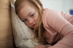 A sad little girl with Down syndrome lying on bed at home.