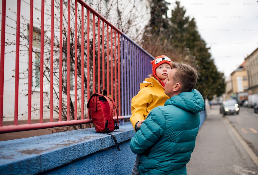 A father taking his little daughter with Down syndrome to school, outdoors in street.
