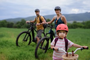 A portrait of excited little girl with her family at backround riding bike on path in park in summer