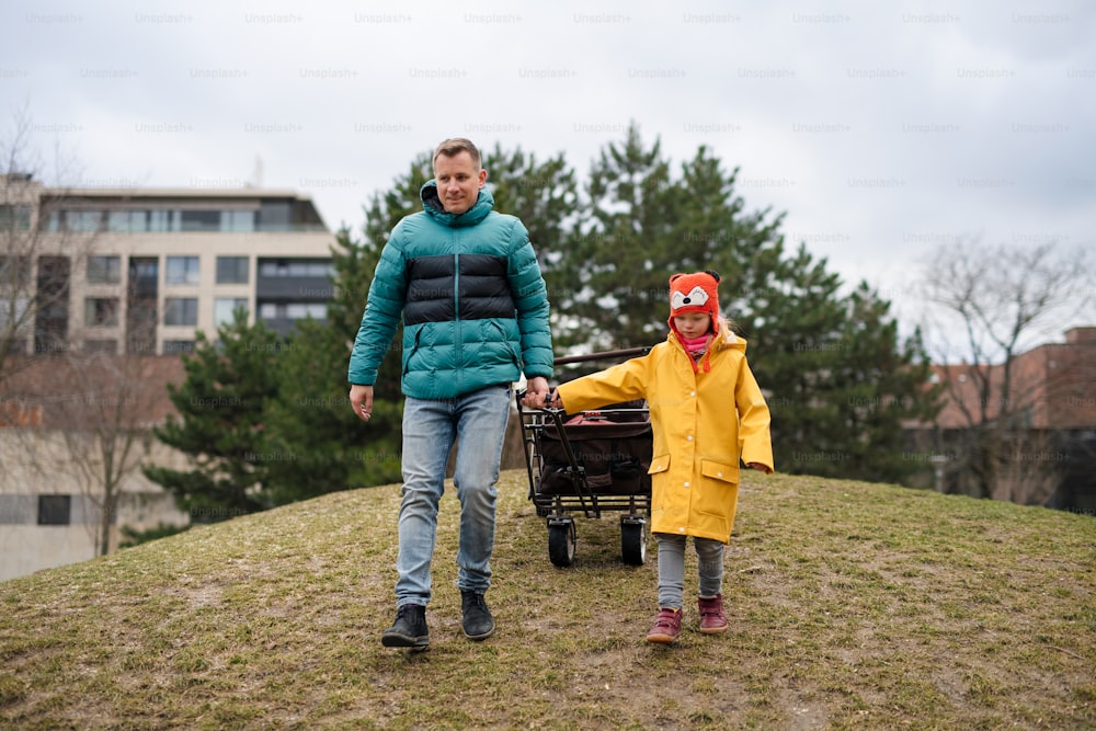Ein Vater mit seiner kleinen Tochter mit Down-Syndrom zieht Trolley draußen im Park.