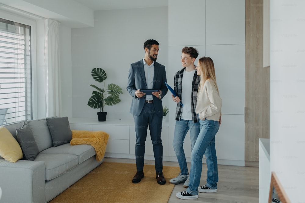A happy young couple buying their new home and meeting real estate agent in apartment.