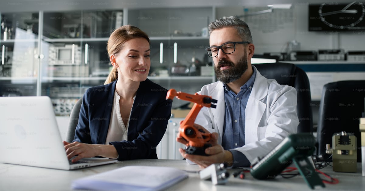 Robotics engineers working on a laptop and desinging modern robotic arm ...