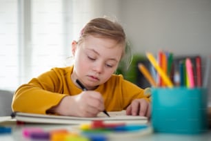 A little girl with Down syndrome drawing at home.