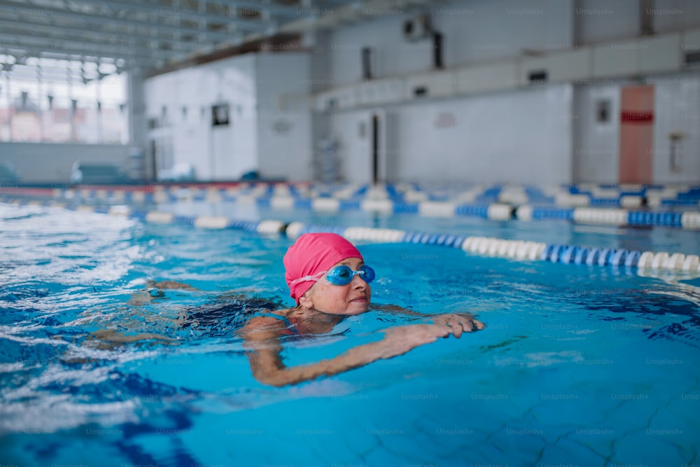 An active senior woman swimming in indoors swimming pool.
