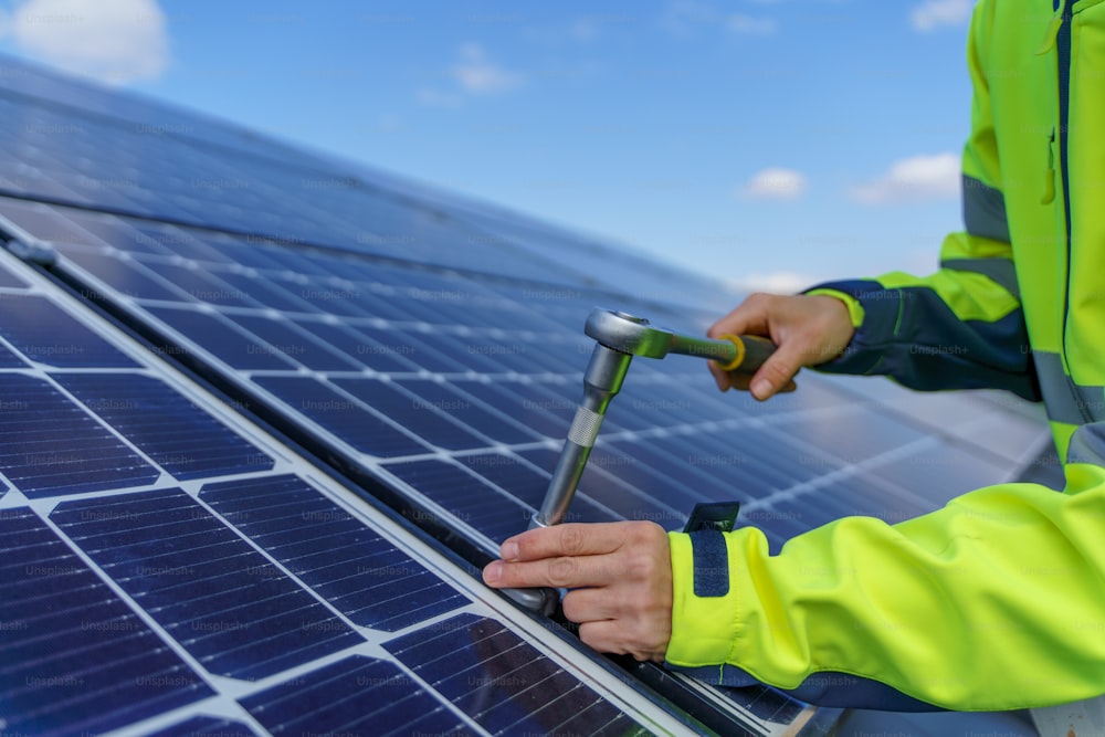 A close-up of woman engineer installing solar photovoltaic panels on roof, alternative energy concept.