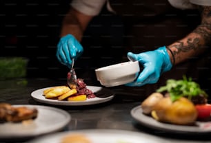 Chef's hands in gloves serving and decorating his meal in restaurant kitchen