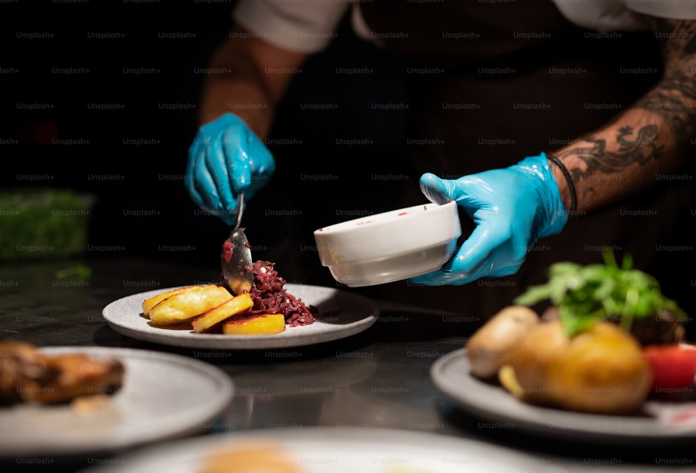 Chef's hands in gloves serving and decorating his meal in restaurant kitchen