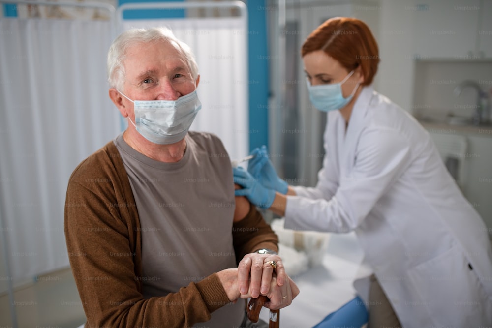 A senior man getting vaccinated in doctor's office, looking at camera.