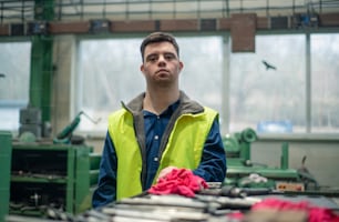 Ein junger Mann mit Down-Syndrom betrachtet Blaupausen bei der Arbeit in einer Industriefabrik, Konzept der sozialen Integration.